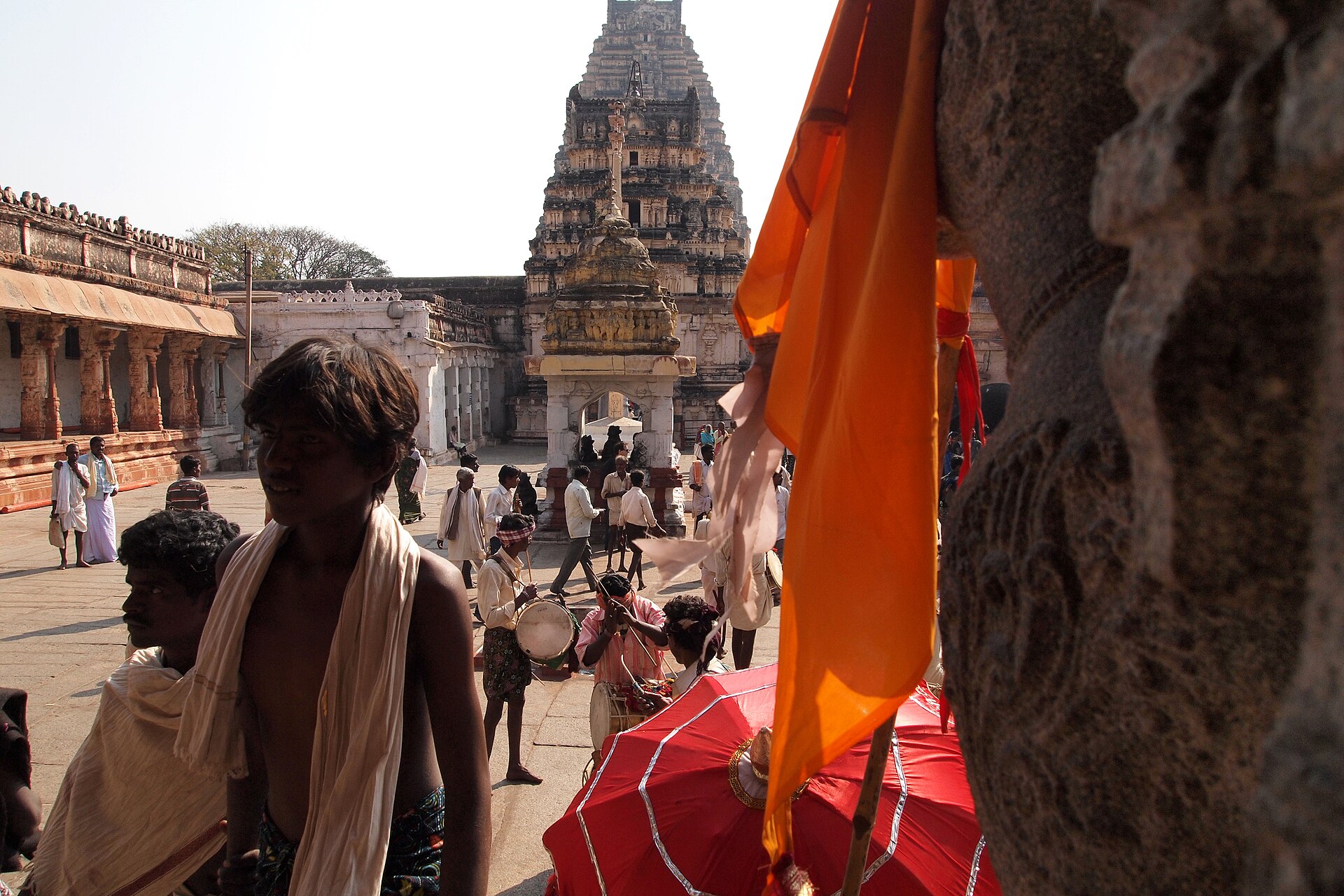 A vibrant Indian temple scene shows musicians performing during a religious procession and devotees gathering, reflecting.