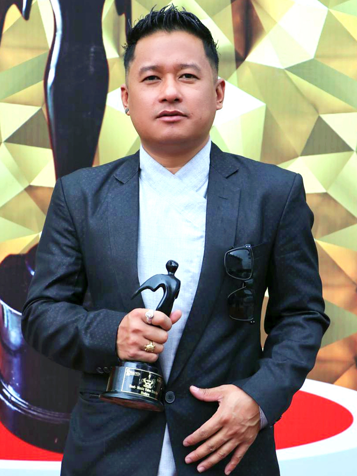 A man in a suit and sunglasses holds an award, representing achievement in indian cinema.